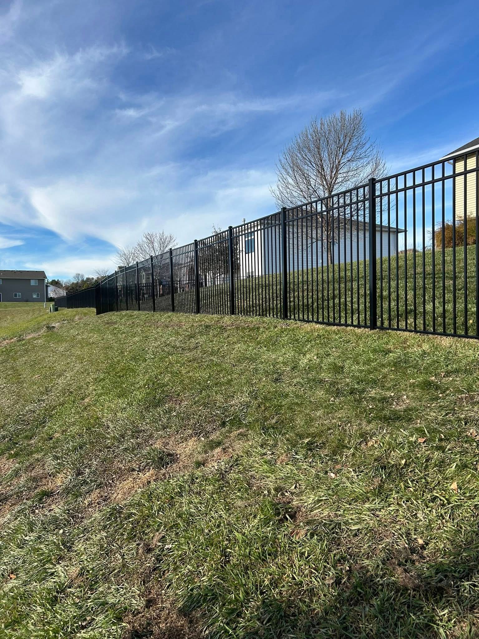 Black metal fence along grassy yard under a blue sky.