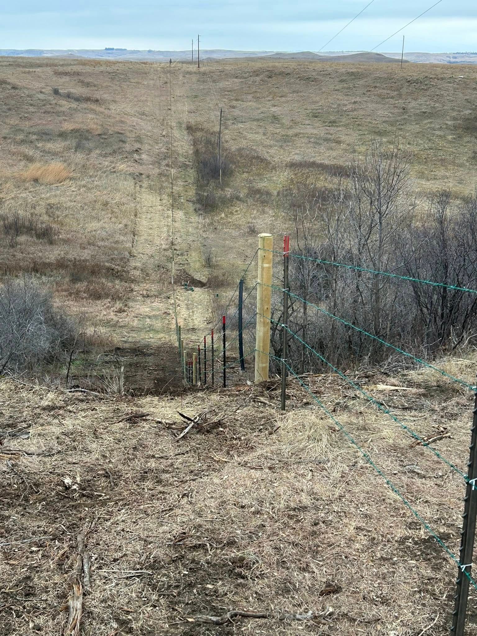 A view of a sandy landscape with a series of stakes and a tall wooden post marked with a flag.