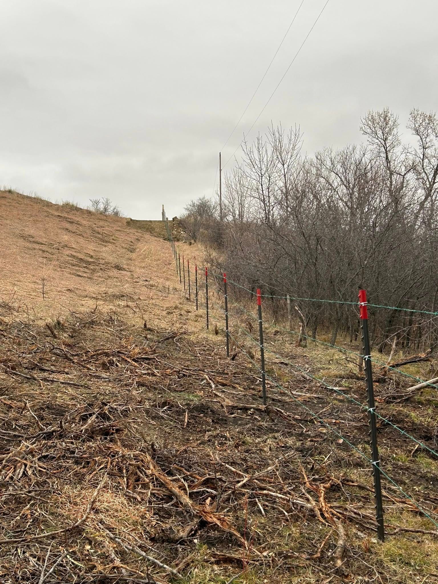 Fence posts with orange markers extend along a grassy hillside under a cloudy sky.
