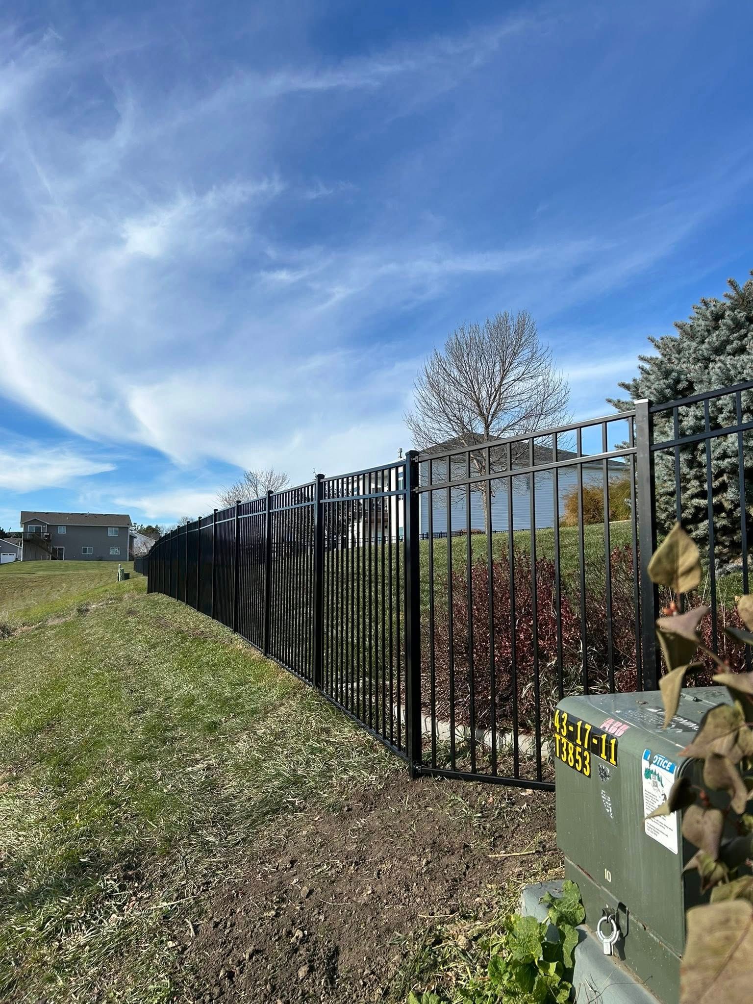 Black metal fence along a grassy area under a partly cloudy sky.