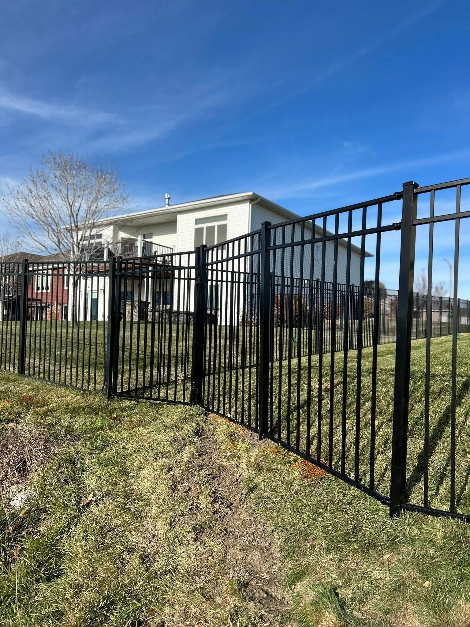 Black metal fence surrounds a white house under a blue sky.