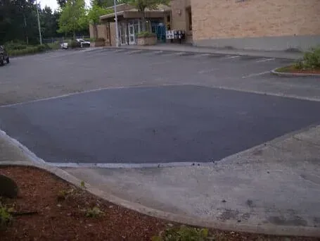 Empty parking lot beside a brick building and sidewalk with landscaping beds