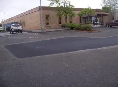 Brick commercial building with parking lot, parked vehicles, and a small tree by the entrance