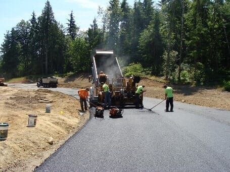 Road paving crew laying asphalt on a rural road with trees in the background