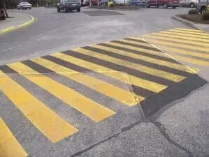 Yellow and black striped speed bump on a paved road near parked cars