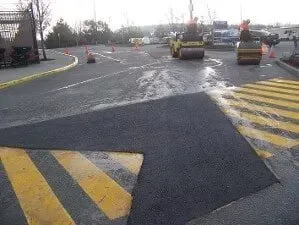 Road work area with two asphalt rollers on a wet street and yellow-black striped markings.