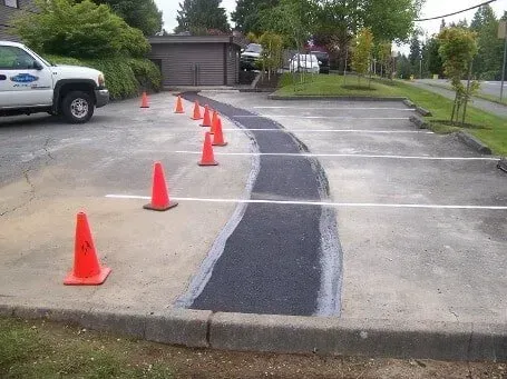 Parking lot curb ramp under construction, marked with orange cones and fresh black asphalt strip