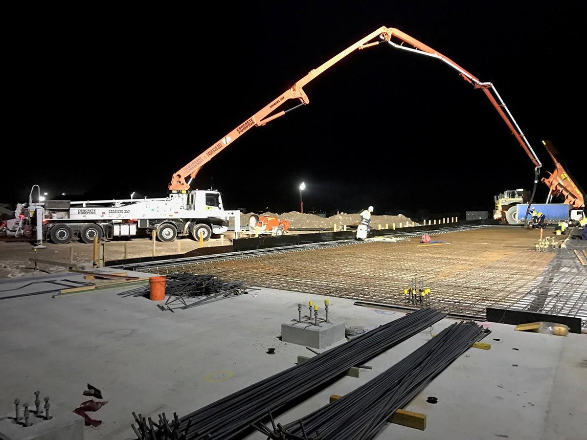 A Concrete Pump is Being Used to Pour Concrete on a Construction Site at Night — Heritage Concrete In Uralla, NSW