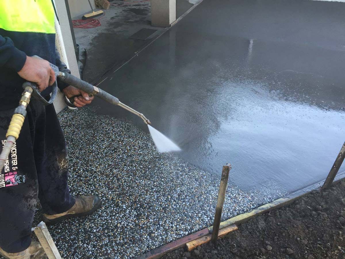 A Man is Spraying Concrete With a High Pressure Washer — Heritage Concrete In Uralla, NSW