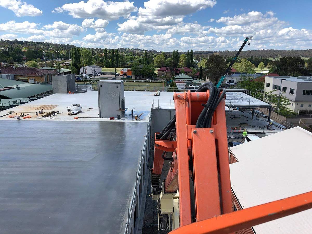 A Large Orange Crane is Sitting on Top of a Building — Heritage Concrete In Uralla, NSW