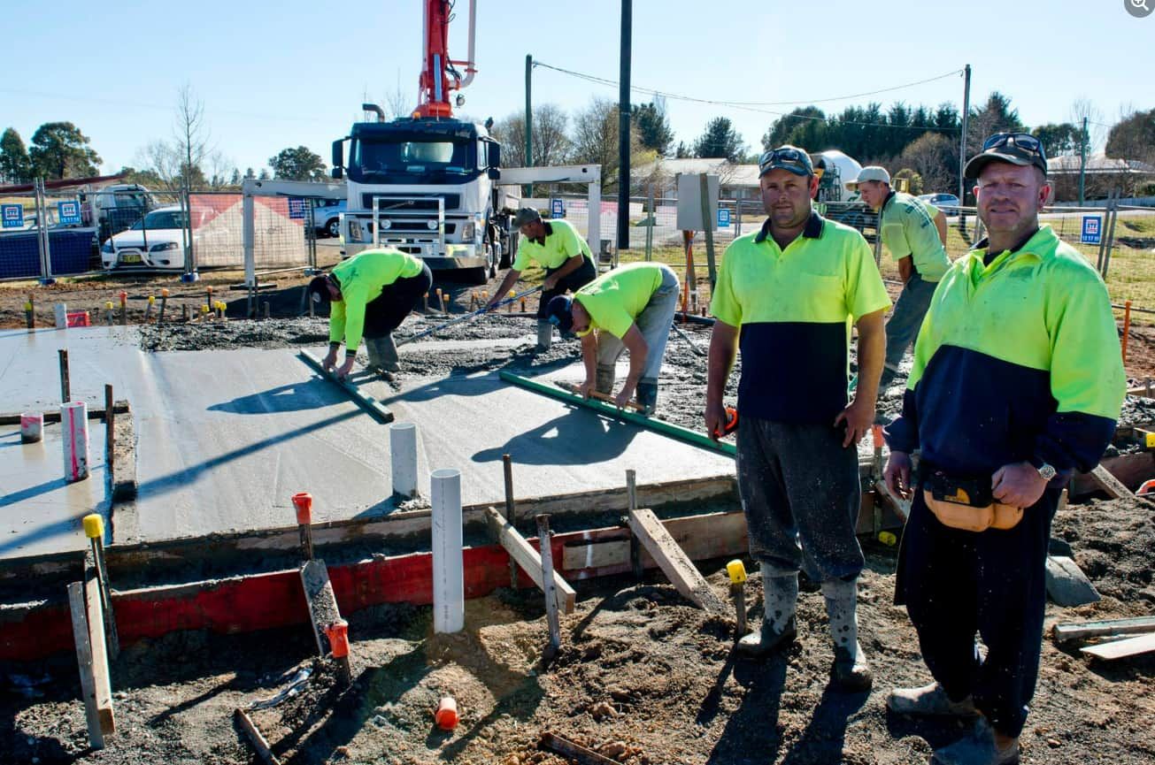 A Group Of Construction Workers Are Standing In Front Of A Concrete Pump — Heritage Concrete In Uralla, NSW
