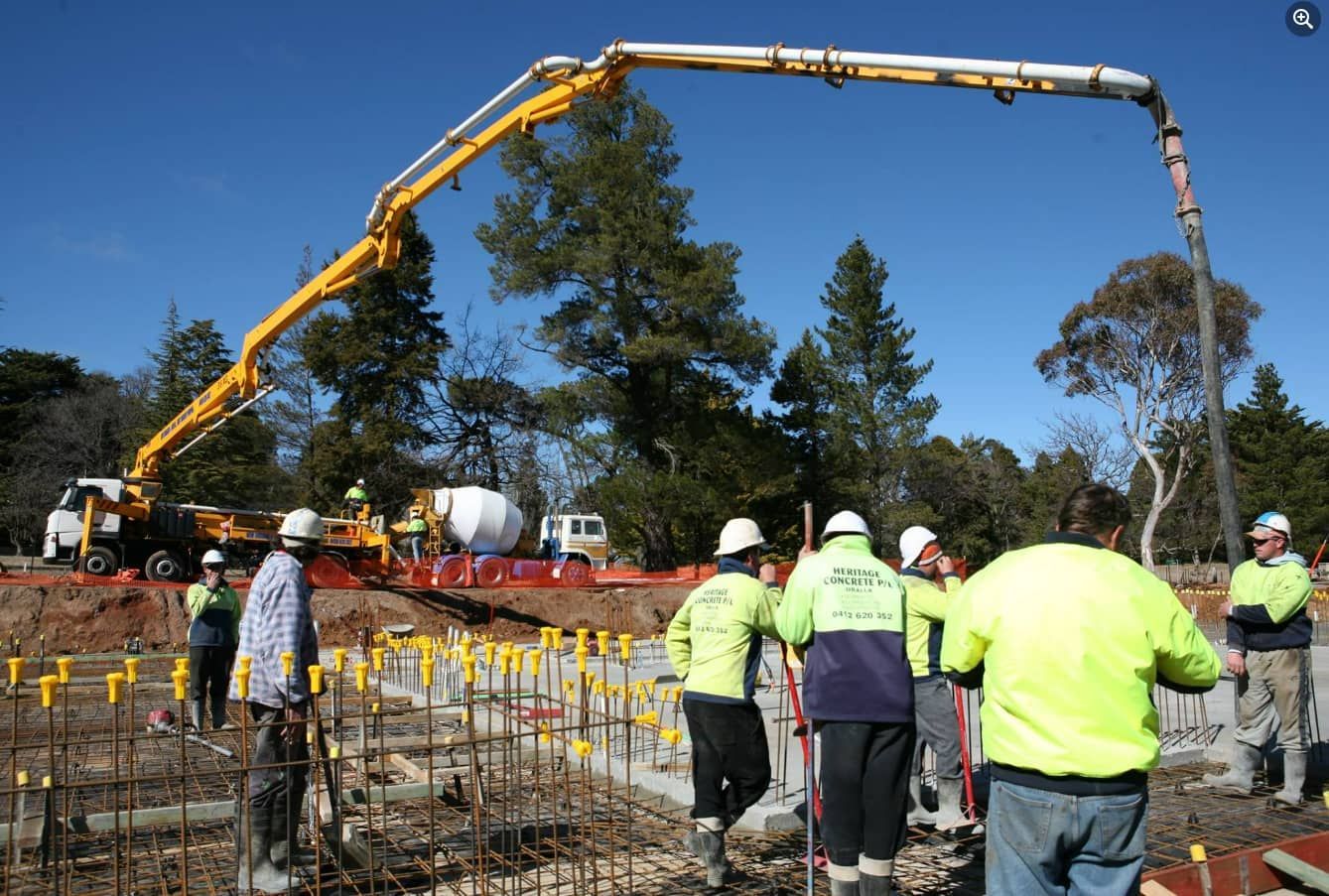 A Group Of Construction Workers Are Standing In Front Of A Concrete Pump — Heritage Concrete In Tamworth, NSW