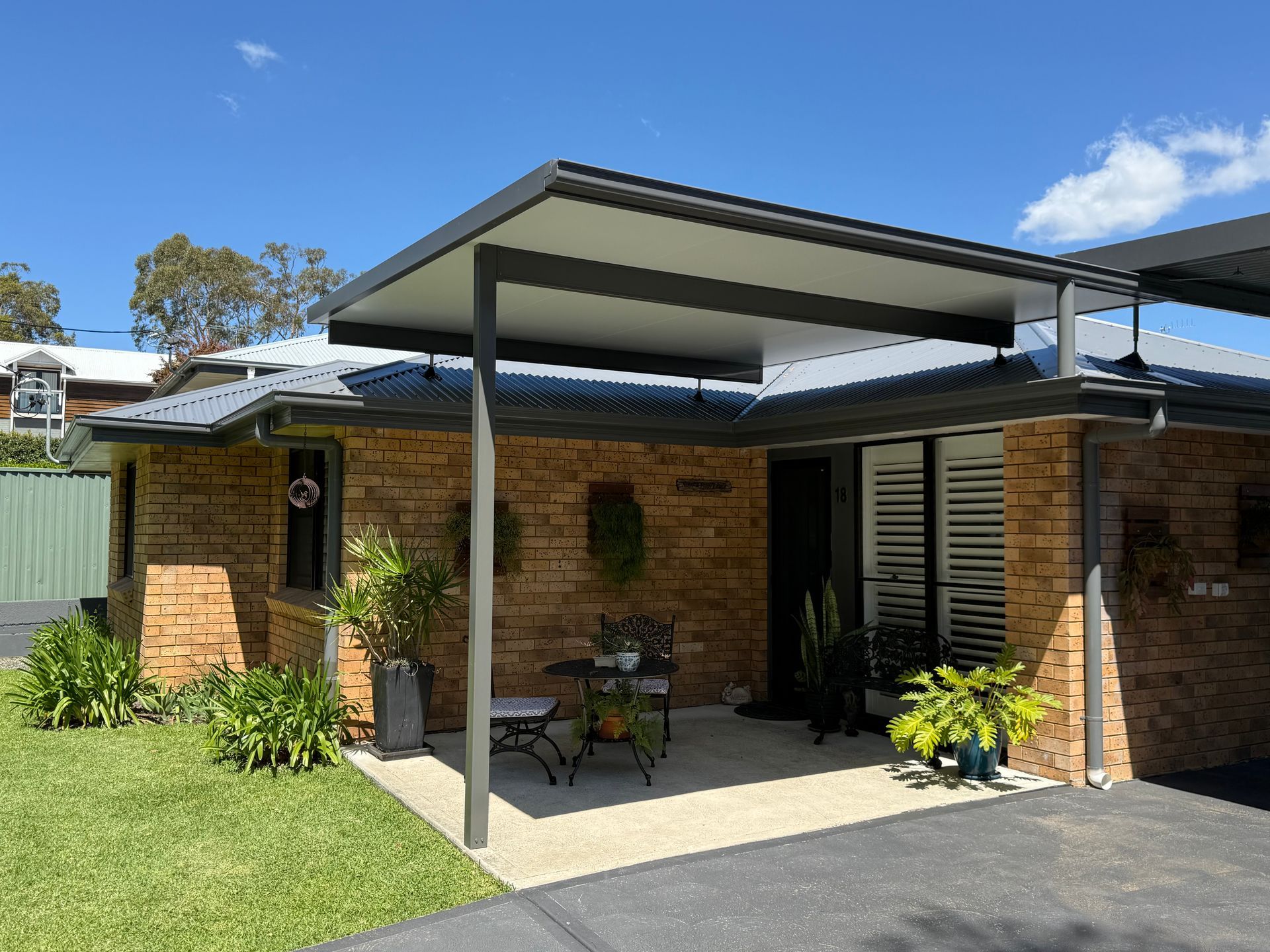 Brick house with covered patio and potted plants under a blue sky.