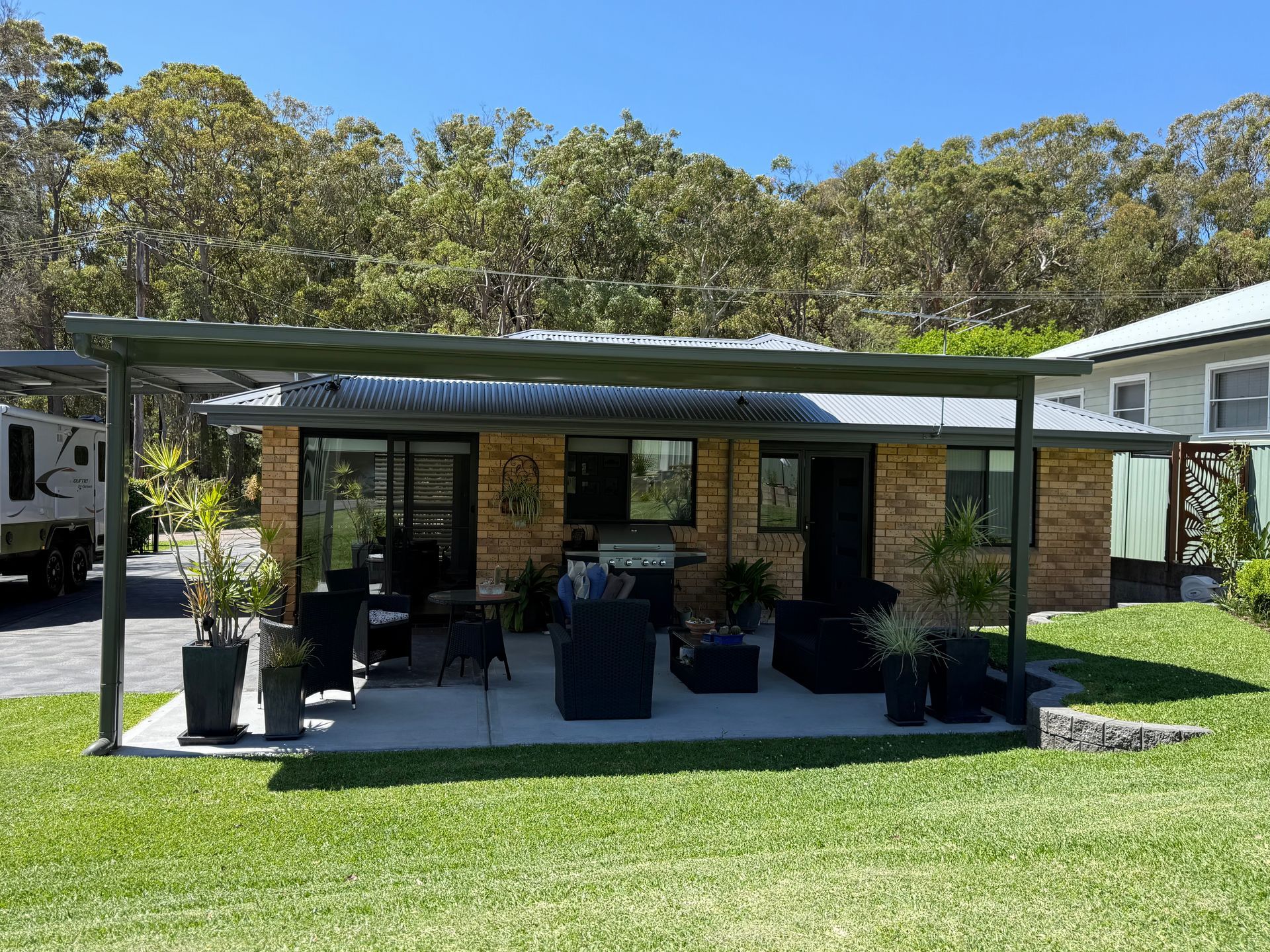 Patio with awning, brick building, outdoor seating, barbecue, and lawn.