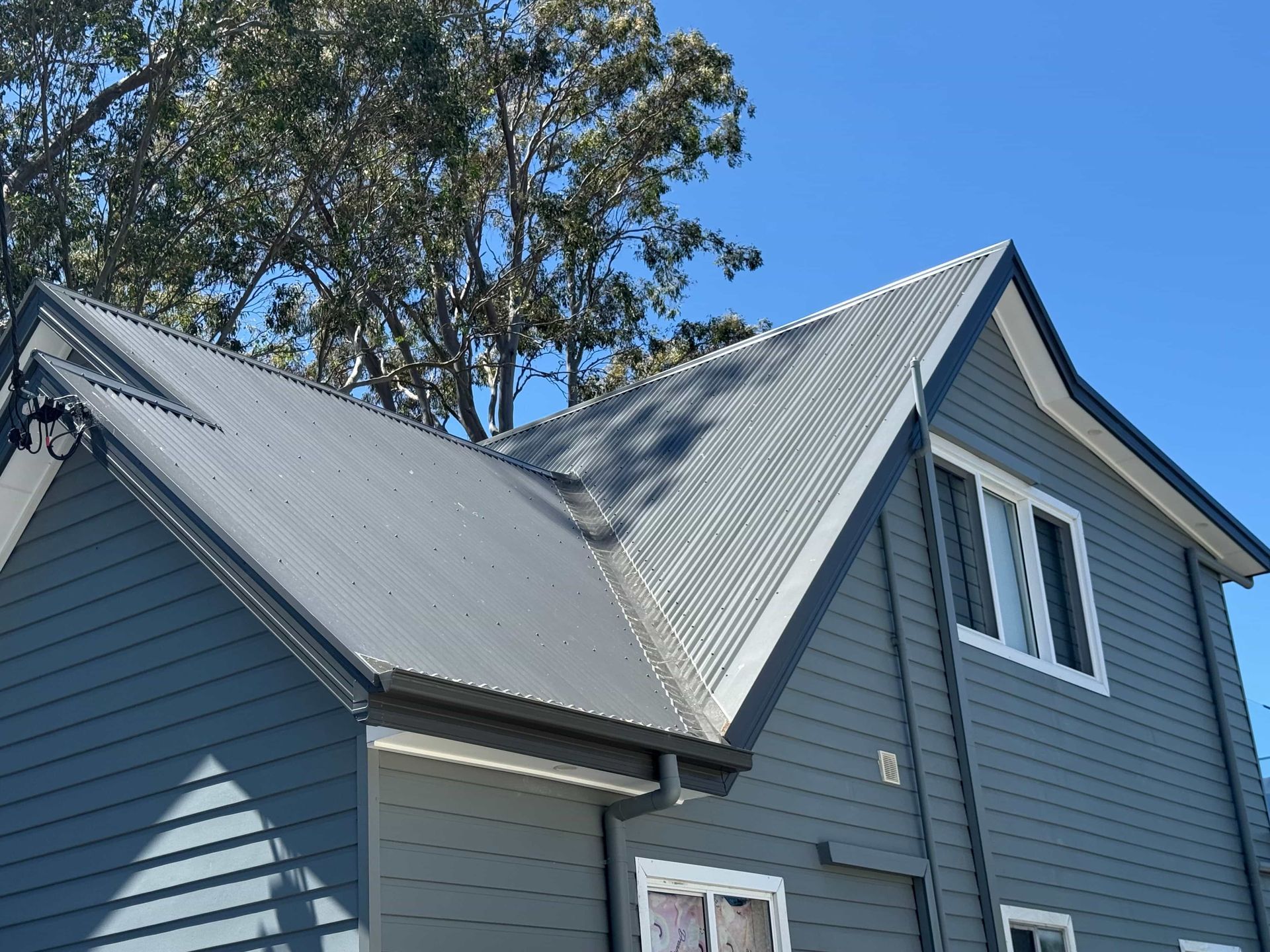 Blue house with gray metal roof, white window trim, and a clear blue sky.