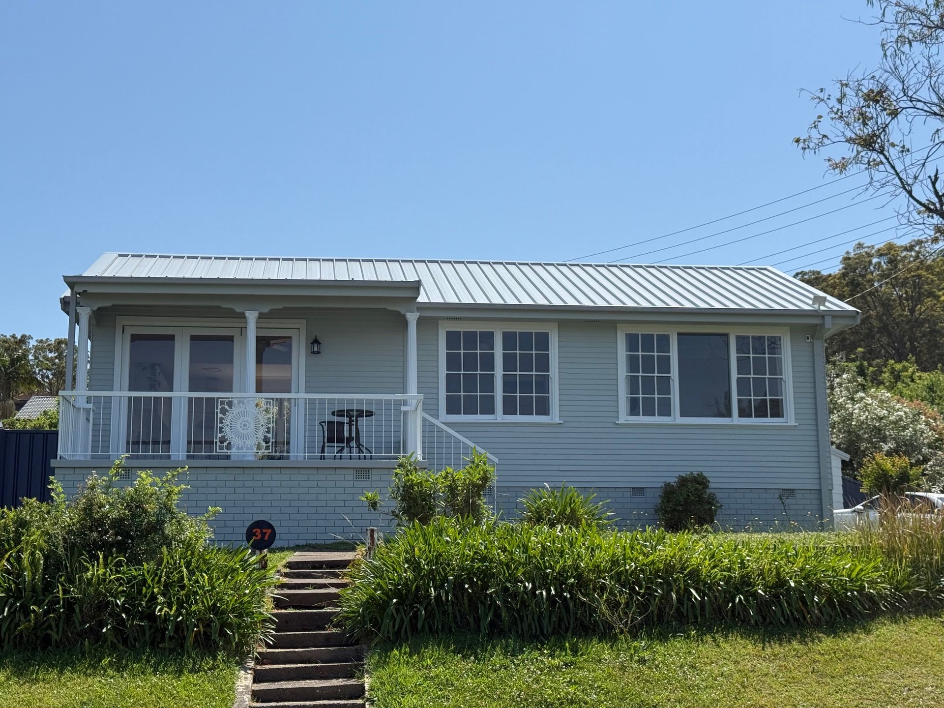 Blue house with white trim, porch, and metal roof under a blue sky.