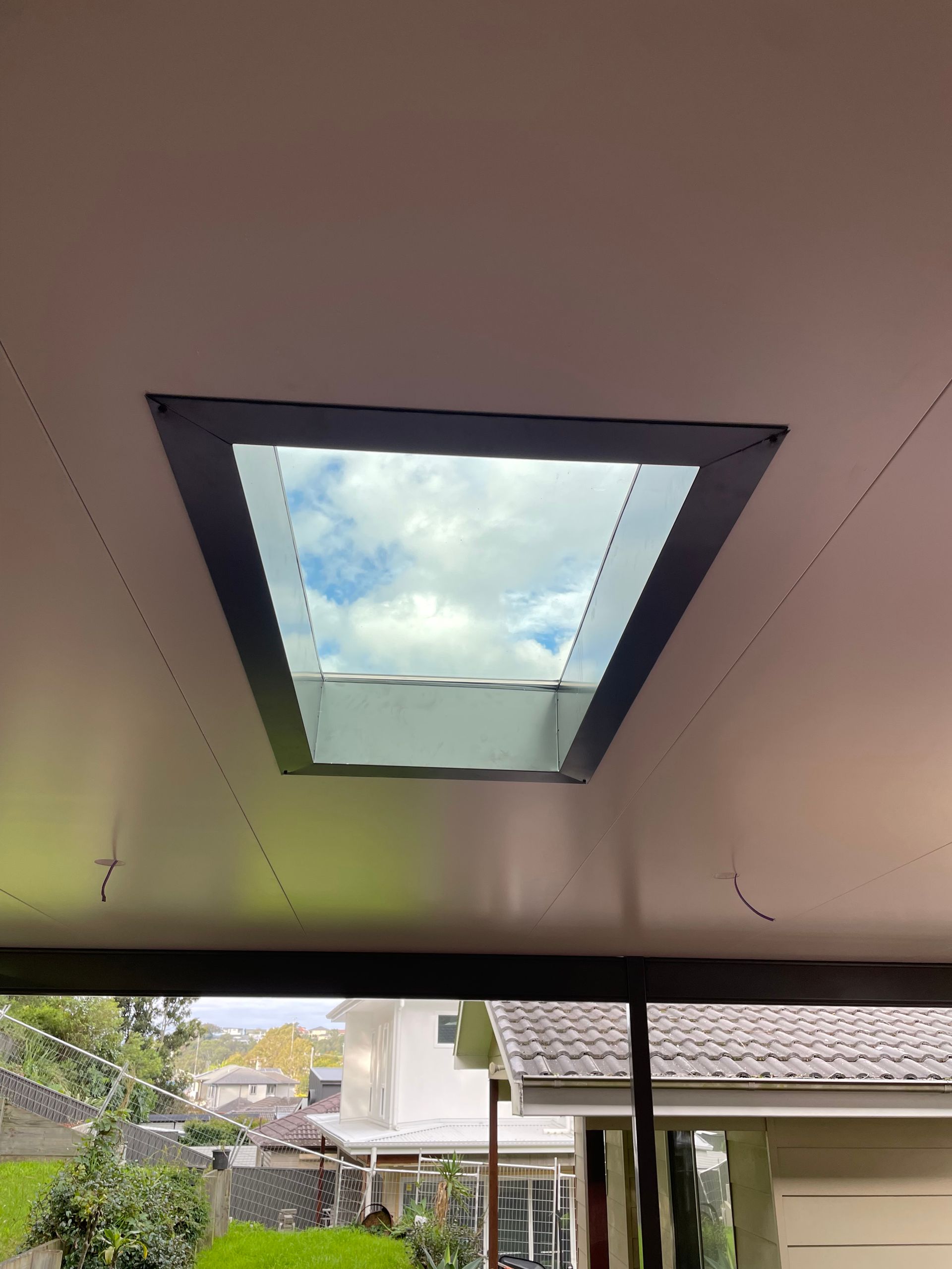 Skylight in a white ceiling, showing a blue sky and clouds. Viewed from below, surrounded by a dark frame.