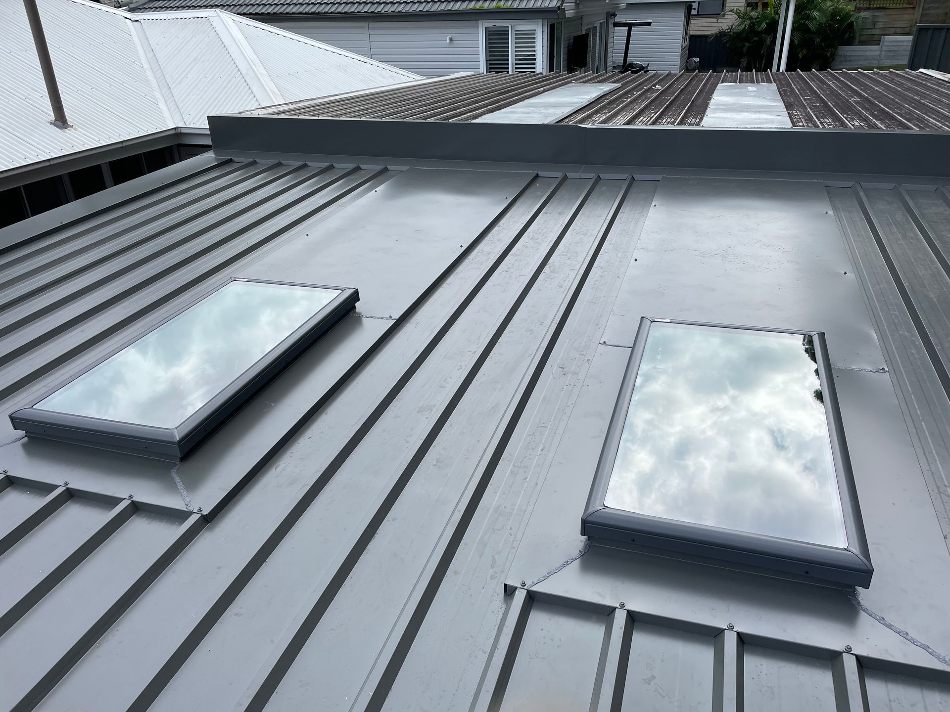 Gray metal roof with two rectangular skylights reflecting the sky.