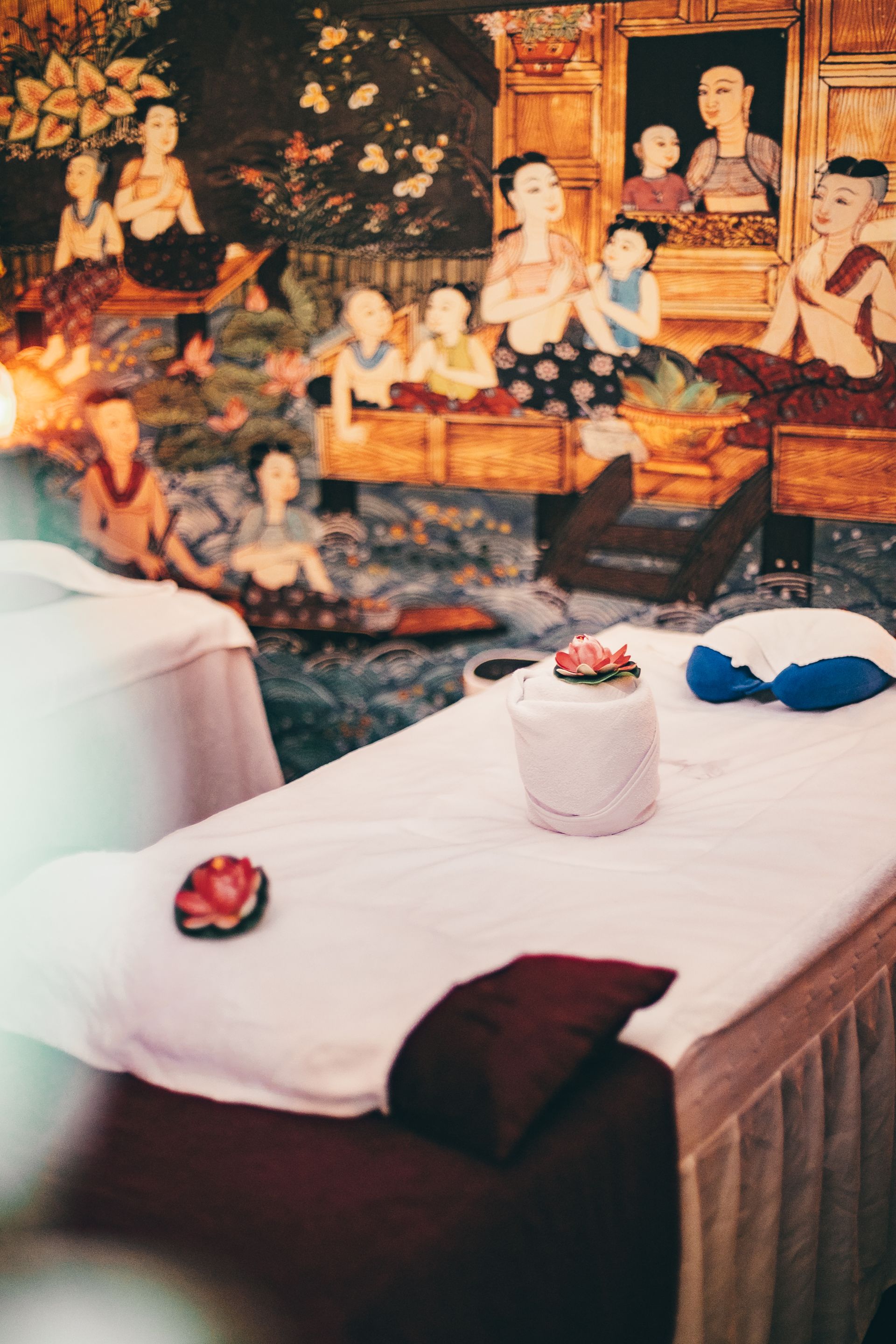 Massage table with white sheets, in front of a painted mural with figures.