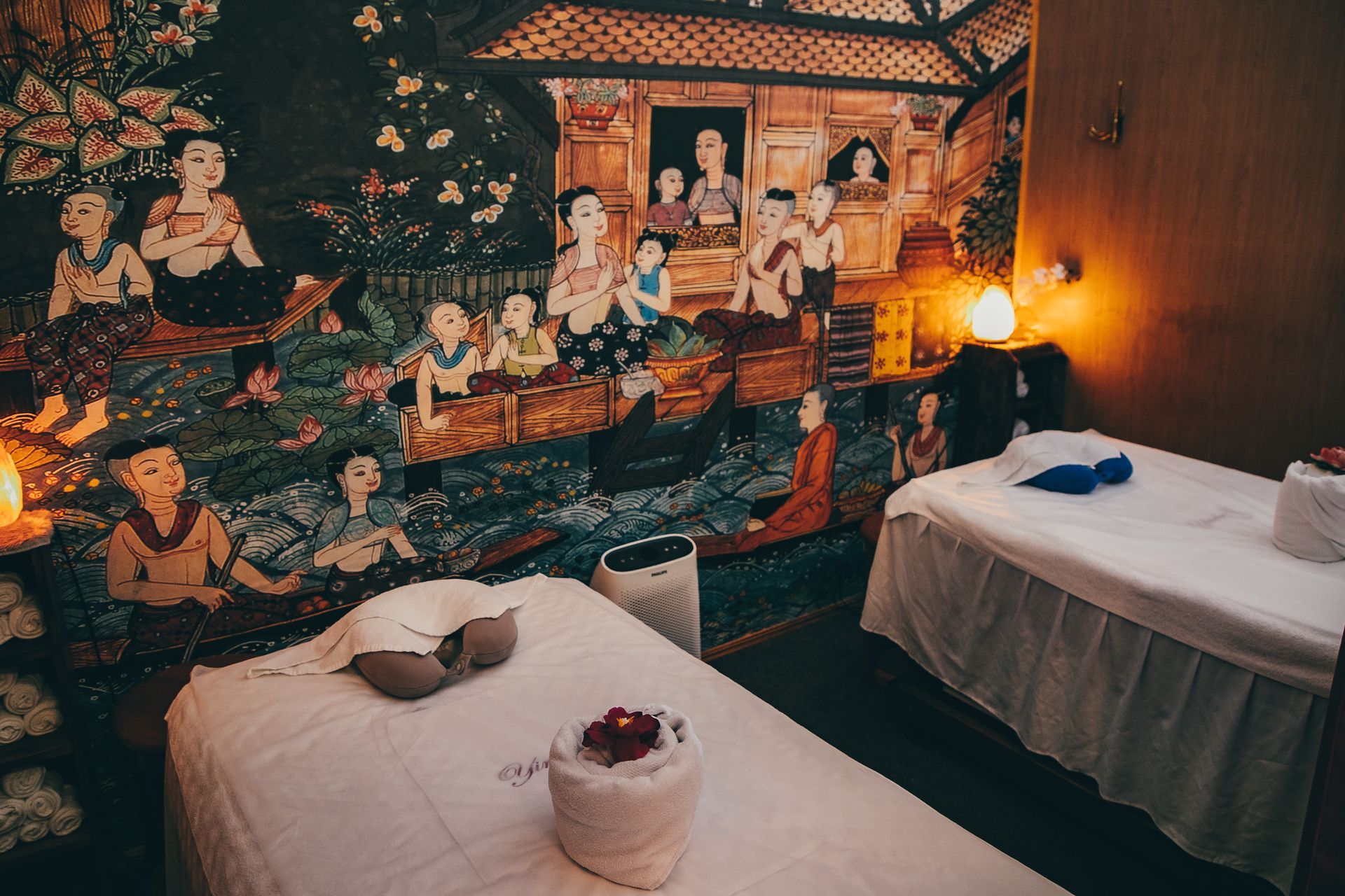 Massage room with two beds and a mural of people. Soft lighting.