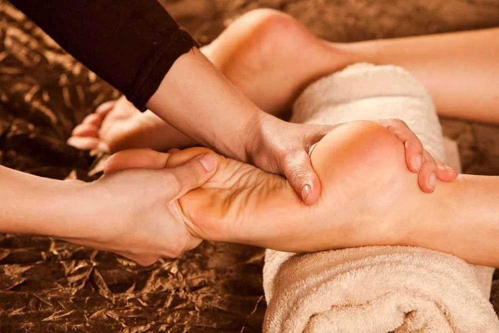 Hands Massaging a Foot Resting on a Rolled White Towel — Traditional Massage Services In Broadbeach, QLD