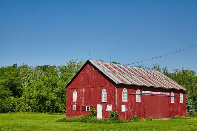 Red barn with white trim in a grassy field under a clear blue sky