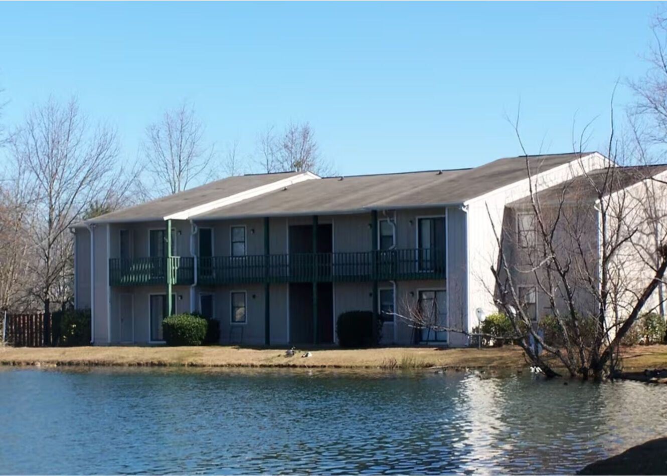 Two-story apartment building next to a pond on a sunny day.