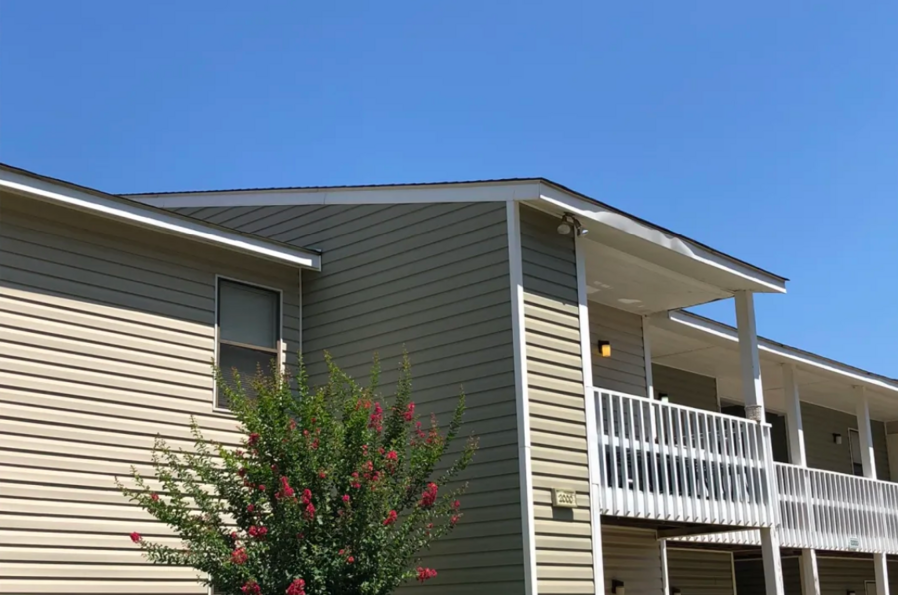 Two-story apartment building with light siding, white trim, and balconies, under a blue sky.