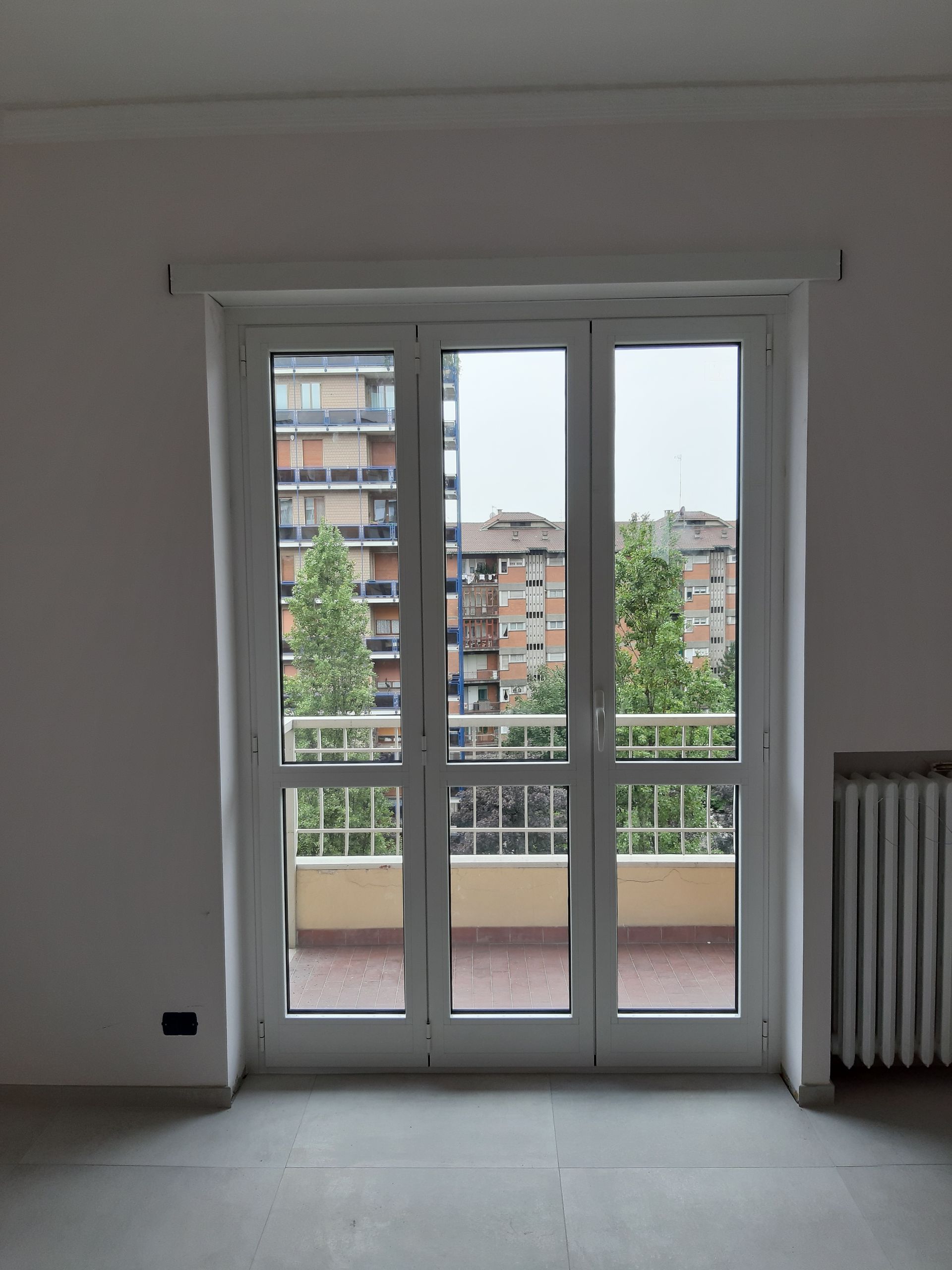 Le porte-finestre bianche si aprono su un balcone con vista su edifici e alberi.