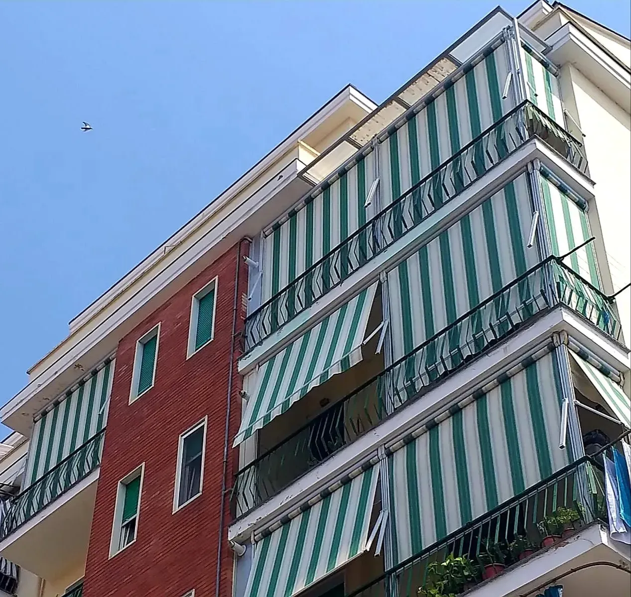 Condominio con tende da sole a strisce verdi e bianche sui balconi; cielo azzurro.