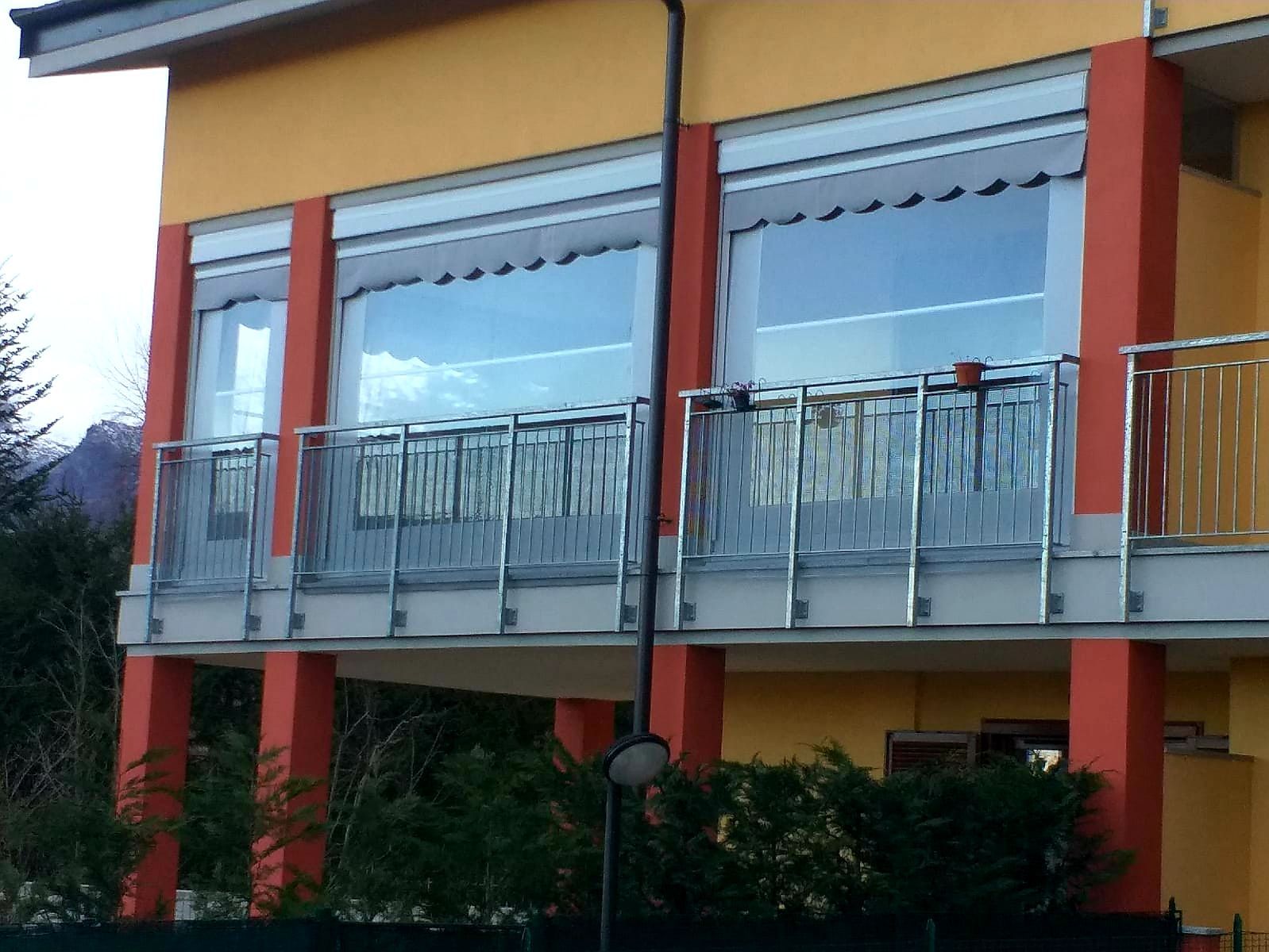 Edificio arancione con balconi, pilastri rossi e grandi finestre che riflettono il cielo.