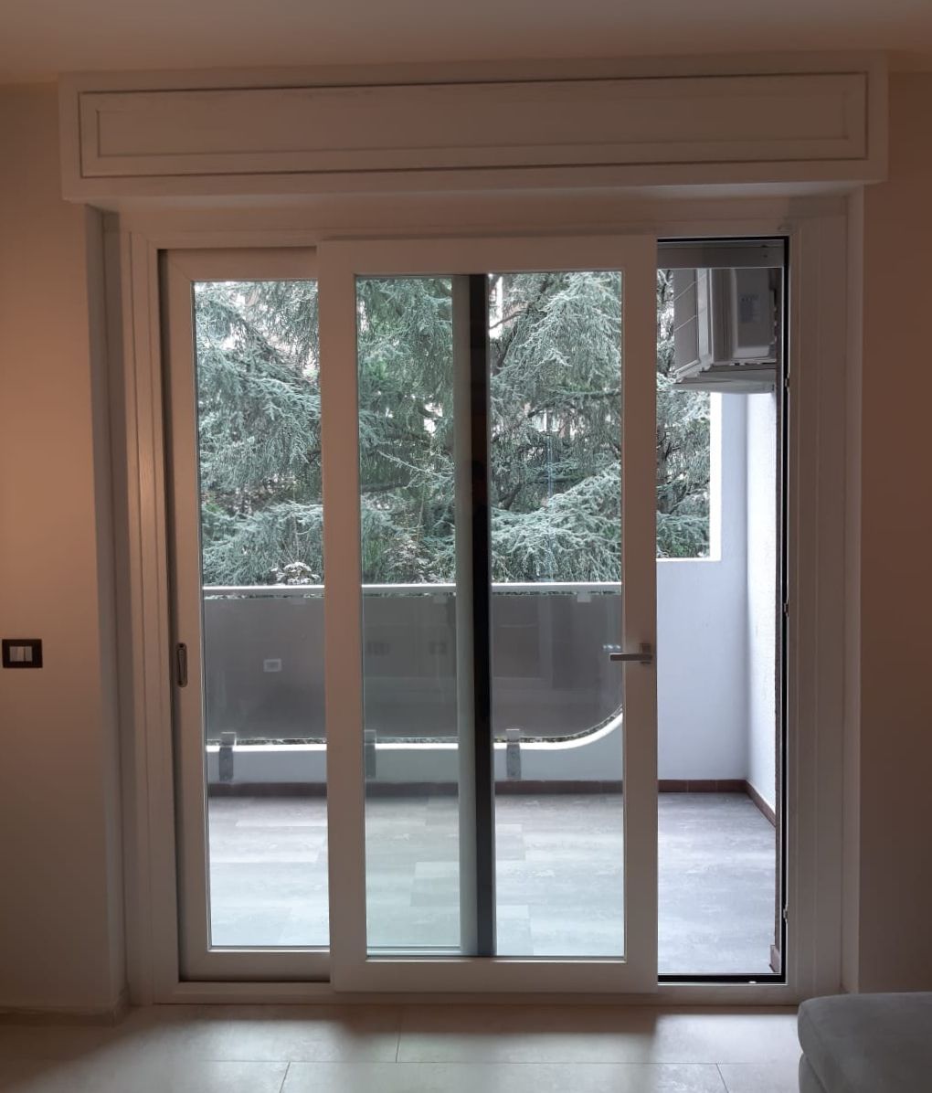 Porta scorrevole in vetro bianco con vista sugli alberi e balcone.