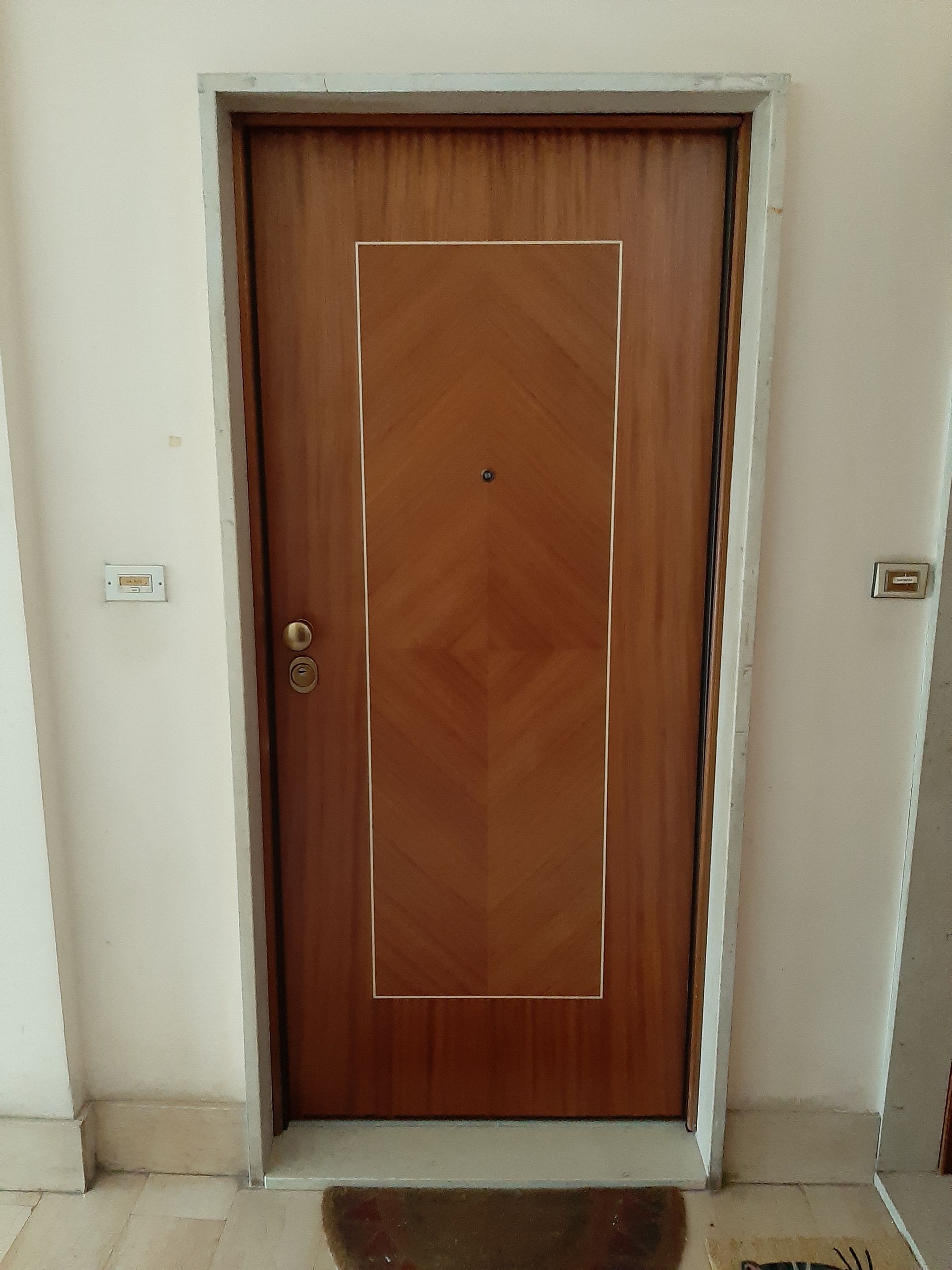 Porta in legno con finiture dorate, inserita in un portale bianco. La porta presenta un motivo a rombi.