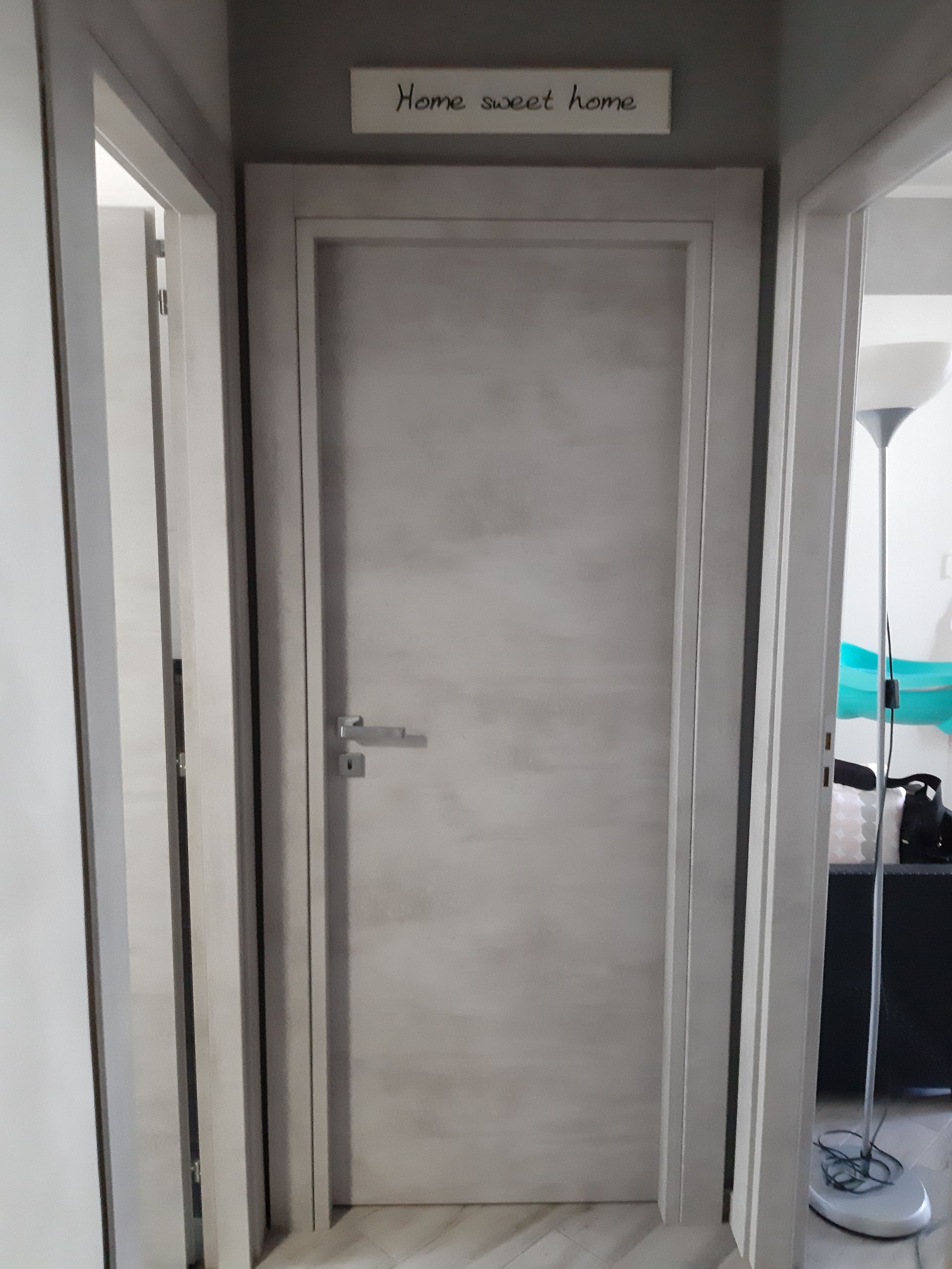 Una porta grigio chiaro con sopra un cartello con la scritta 