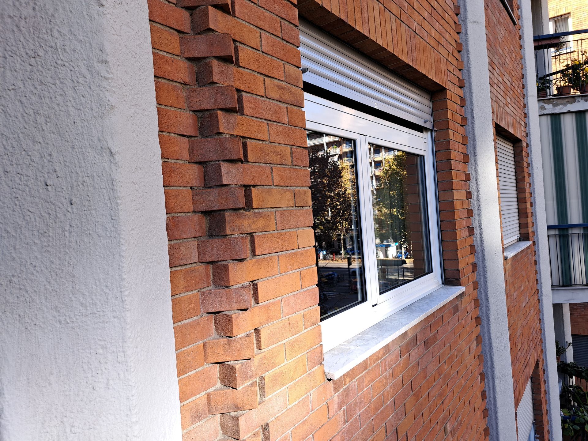 Esterno di un edificio in mattoni con una finestra e mattoni crepati lungo il bordo.