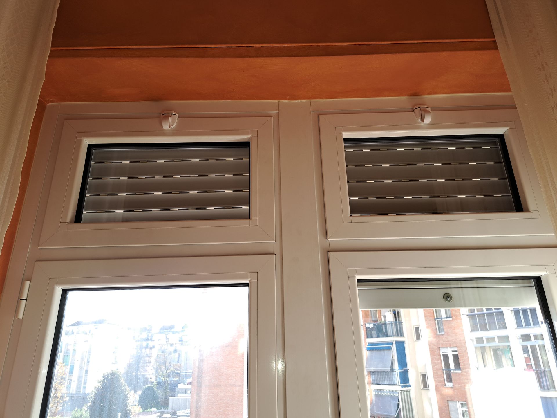 Due finestre con cornice bianca e persiane orizzontali chiuse, soffitto arancione.