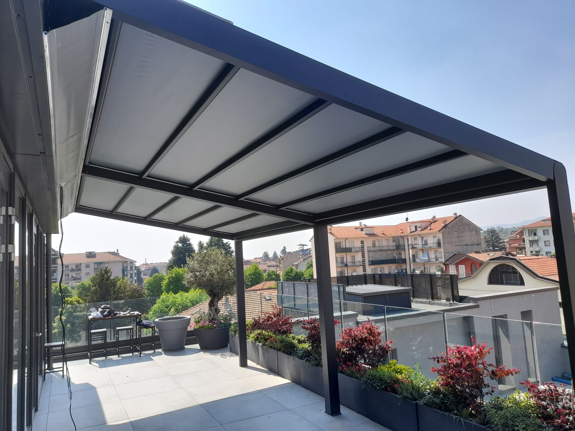 Un patio sul tetto con pergolato retrattile offre ombra a un'area salotto, con il paesaggio urbano sullo sfondo.