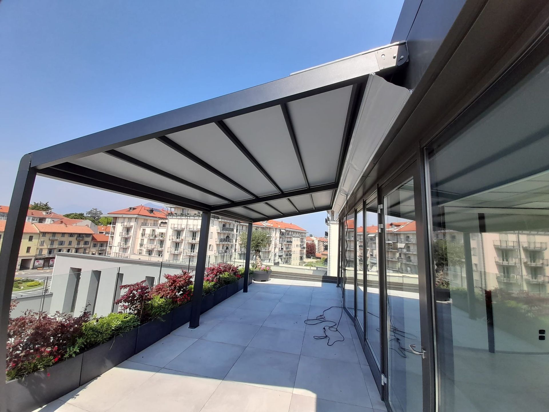 Pergola moderna con tenda da sole bianca retrattile su un patio sul tetto, con vista sugli edifici della città.