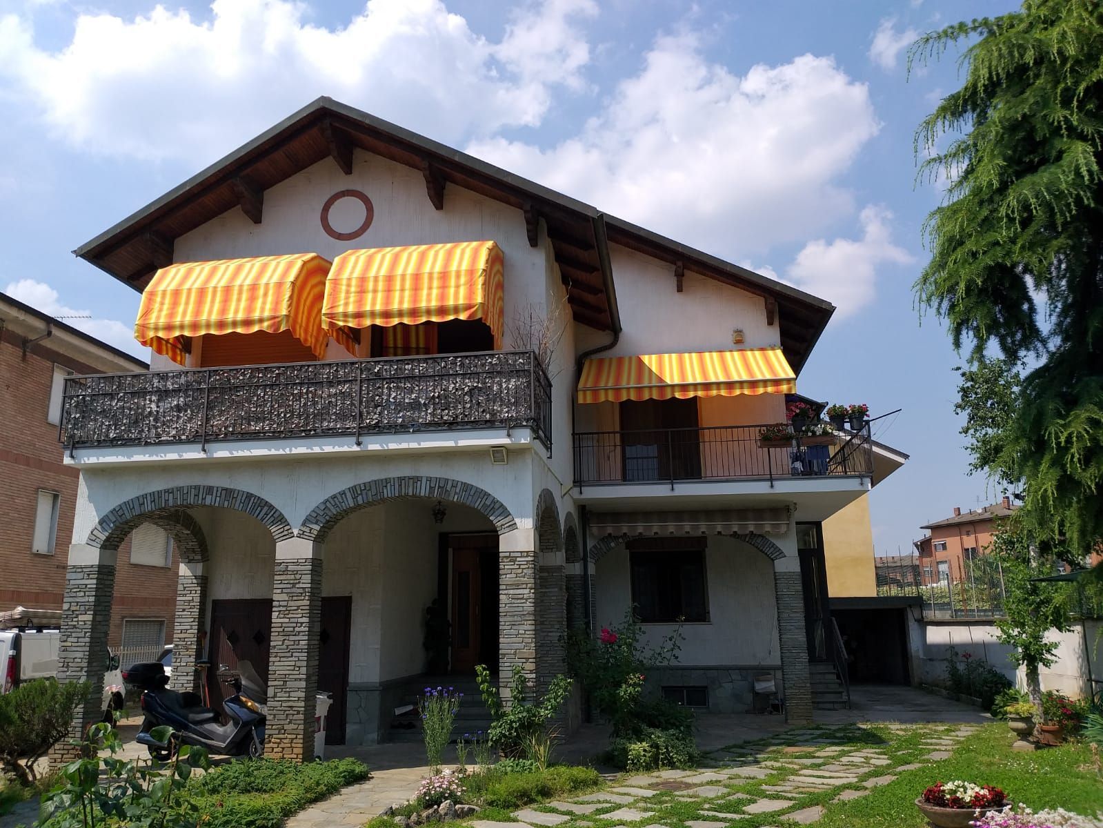 Casa a due piani con tende da sole gialle, archi in pietra e balcone, giornata di sole.