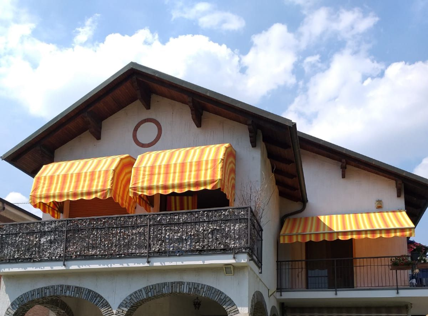 Casa a due piani con tende da sole gialle e facciata in pietra, con uno scooter parcheggiato sotto gli archi.