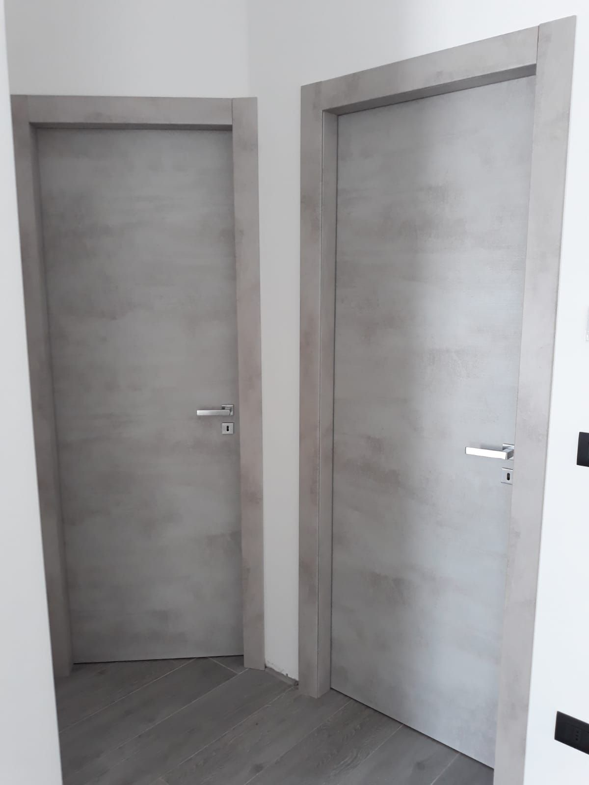 Due porte di legno grigio in un corridoio. Entrambe le porte sono chiuse e hanno maniglie argentate.