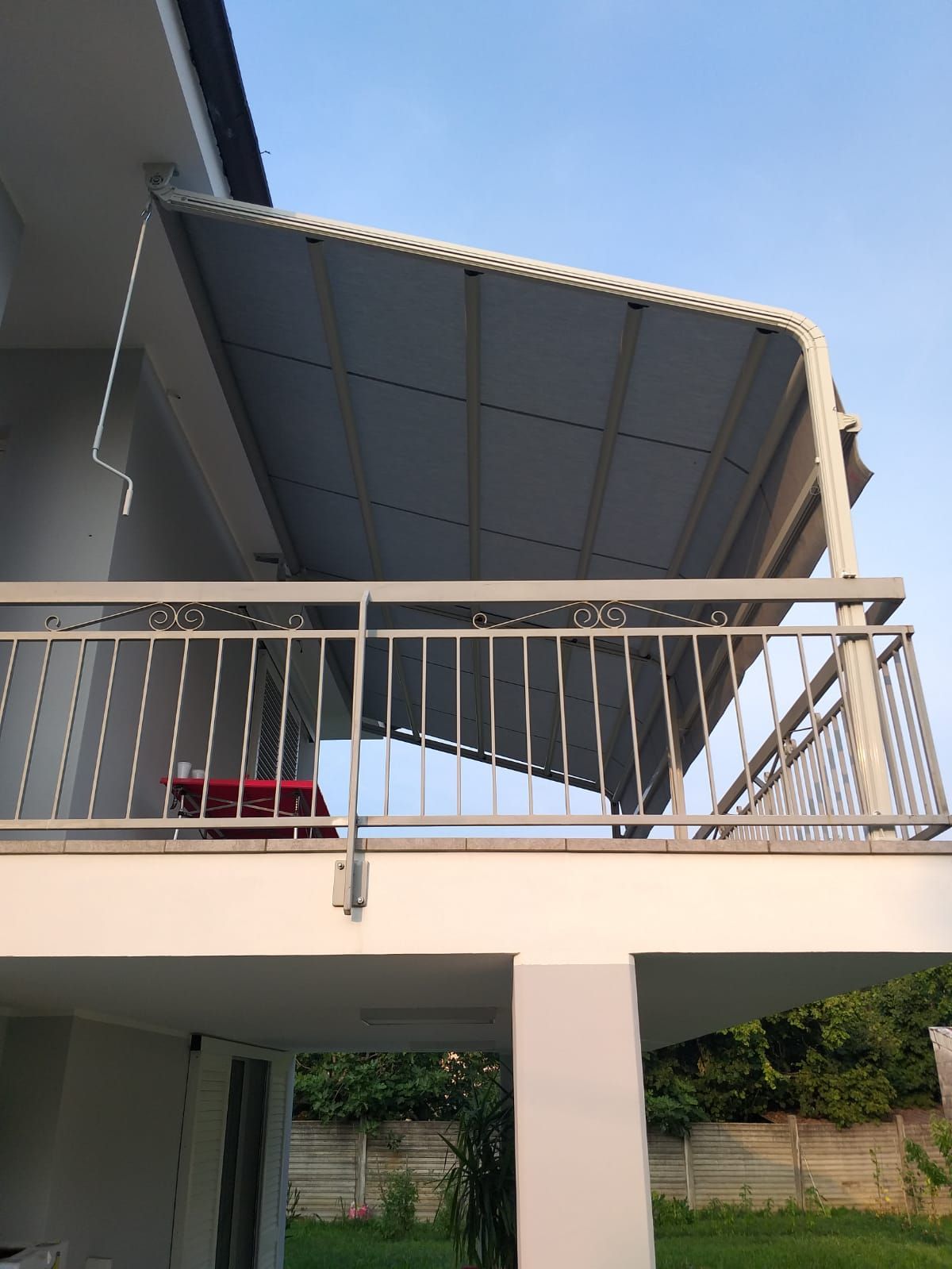 Balcone con tenda da sole grigia sopra una ringhiera, attaccato a un edificio bianco, all'aperto.