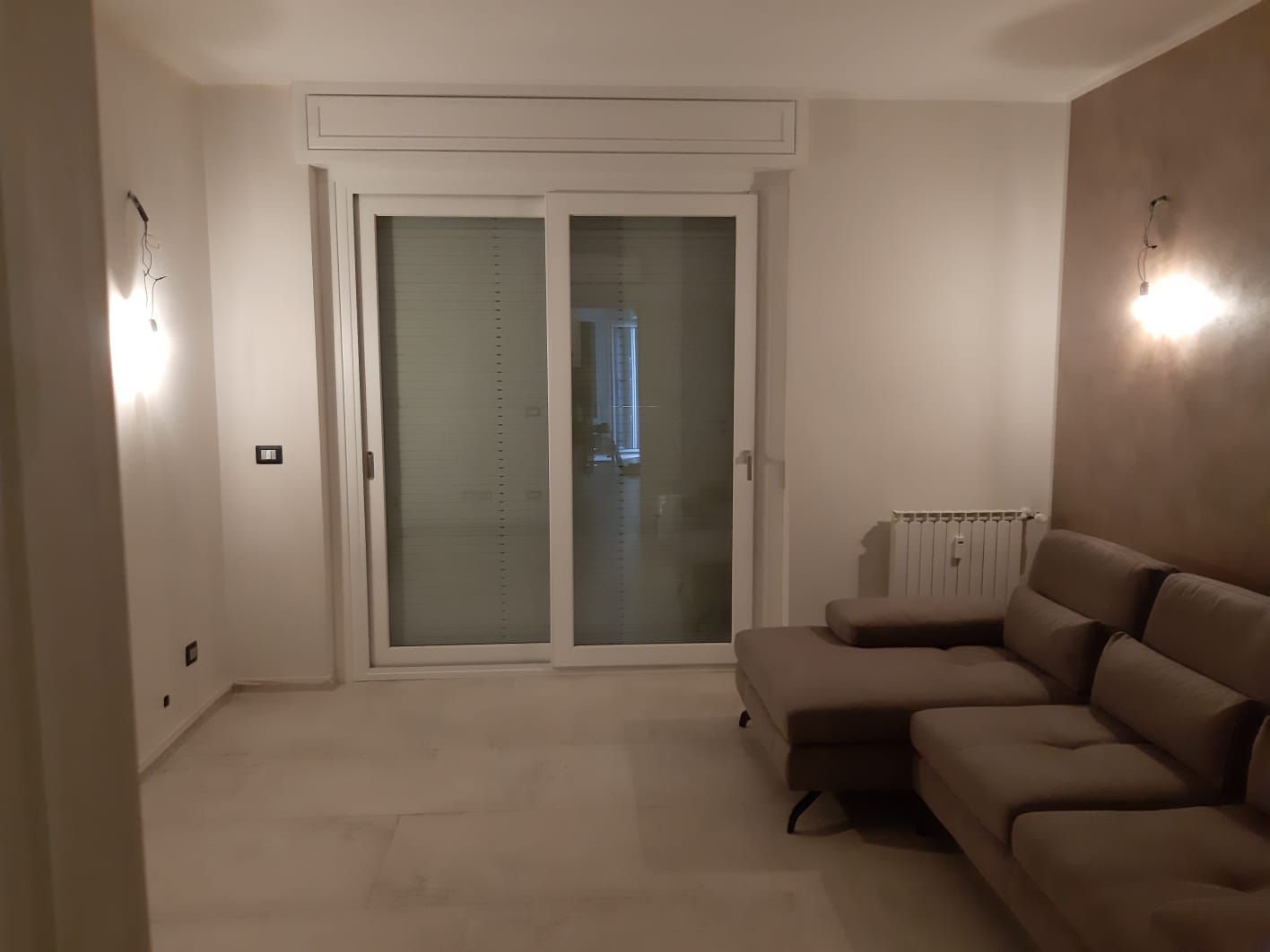 Soggiorno con porta scorrevole in vetro, divano componibile grigio e applique.