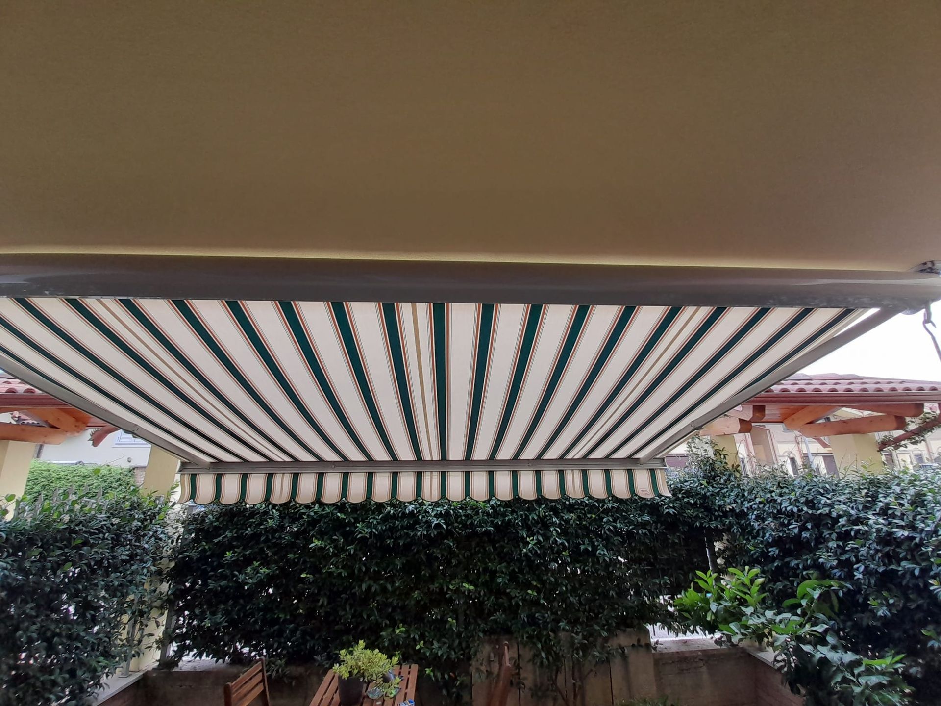 Tenda a strisce su una siepe verde. Strisce bianche e verdi, telo superiore beige.