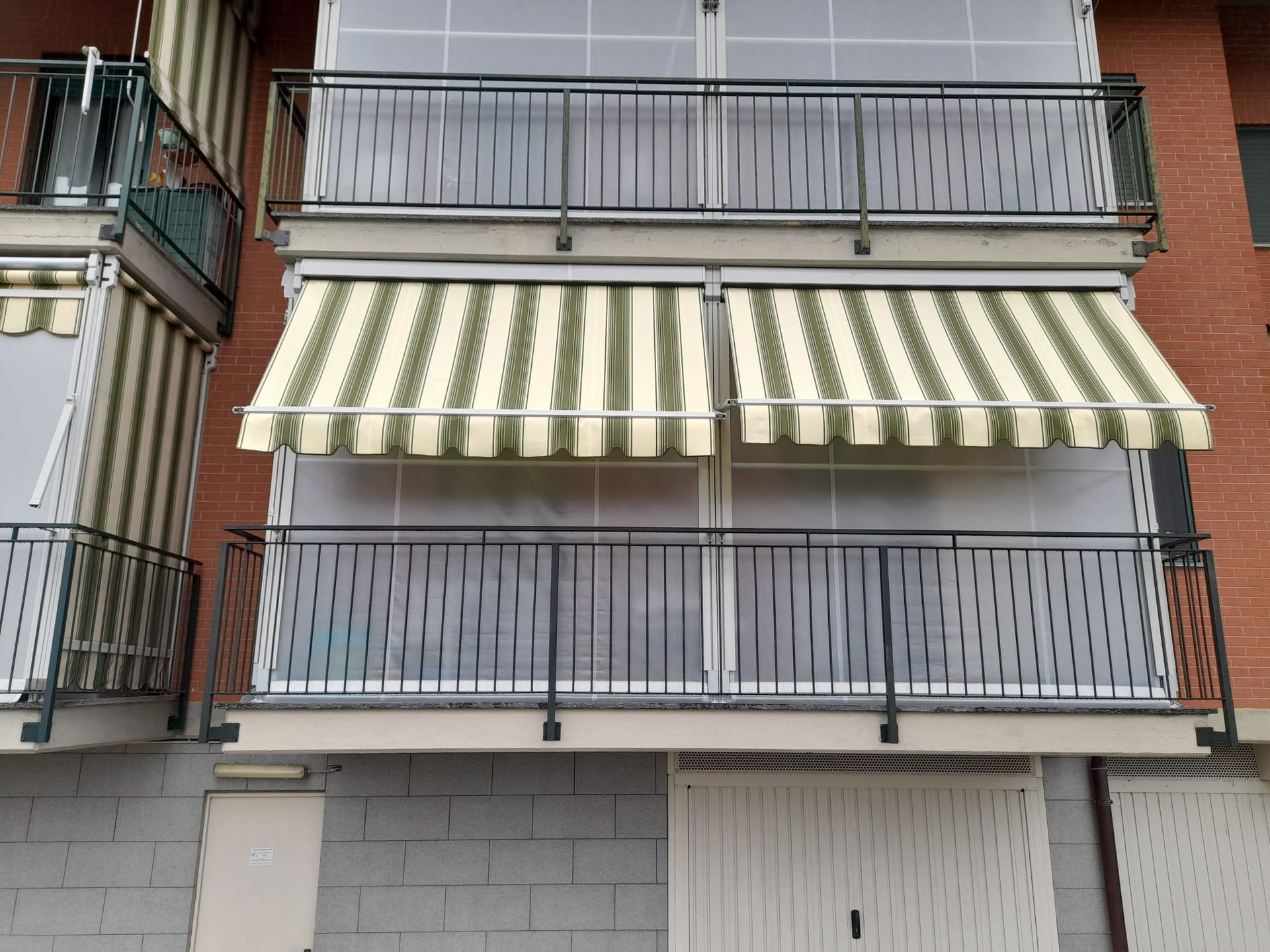 Balconi con tende a strisce e ringhiere nere su un edificio in mattoni.