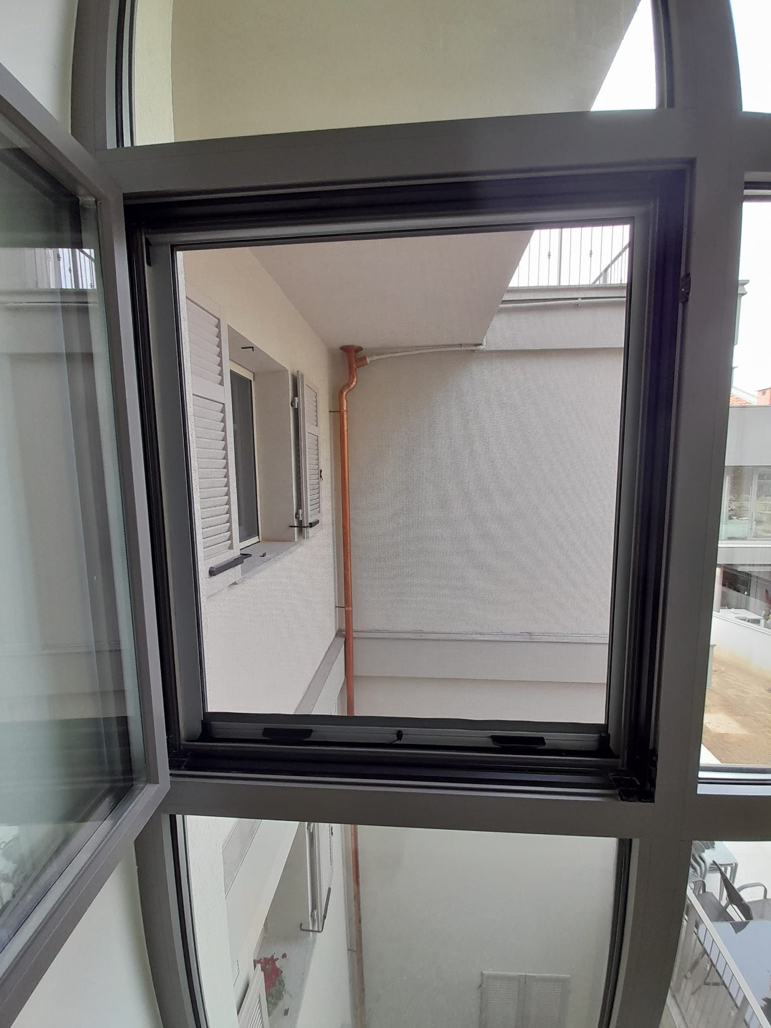 Finestra aperta che si affaccia su un balcone con pareti bianche e una finestra con persiane.