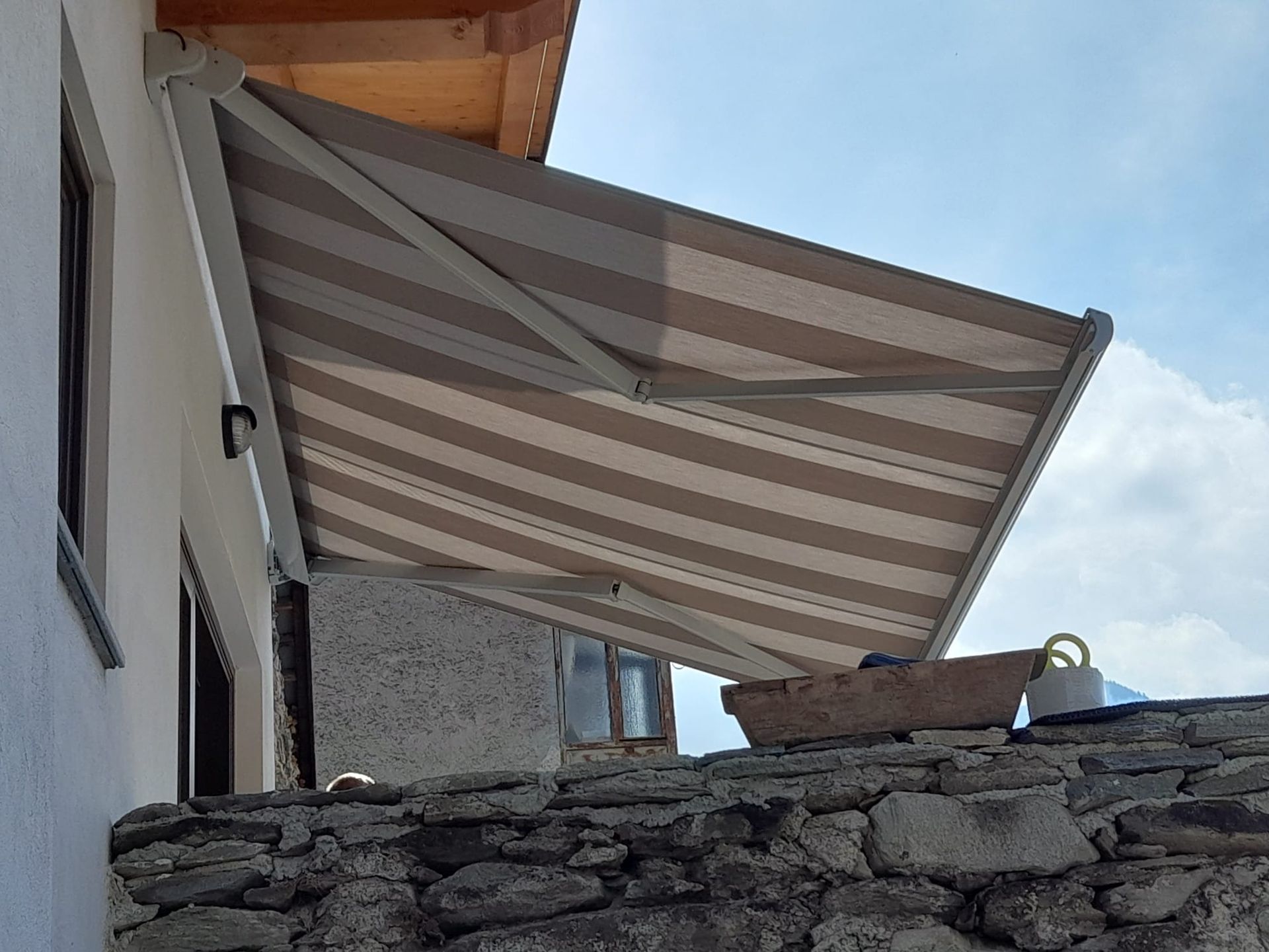 Una tenda a strisce si estendeva da un edificio bianco, proiettando ombra su un muro di pietra.