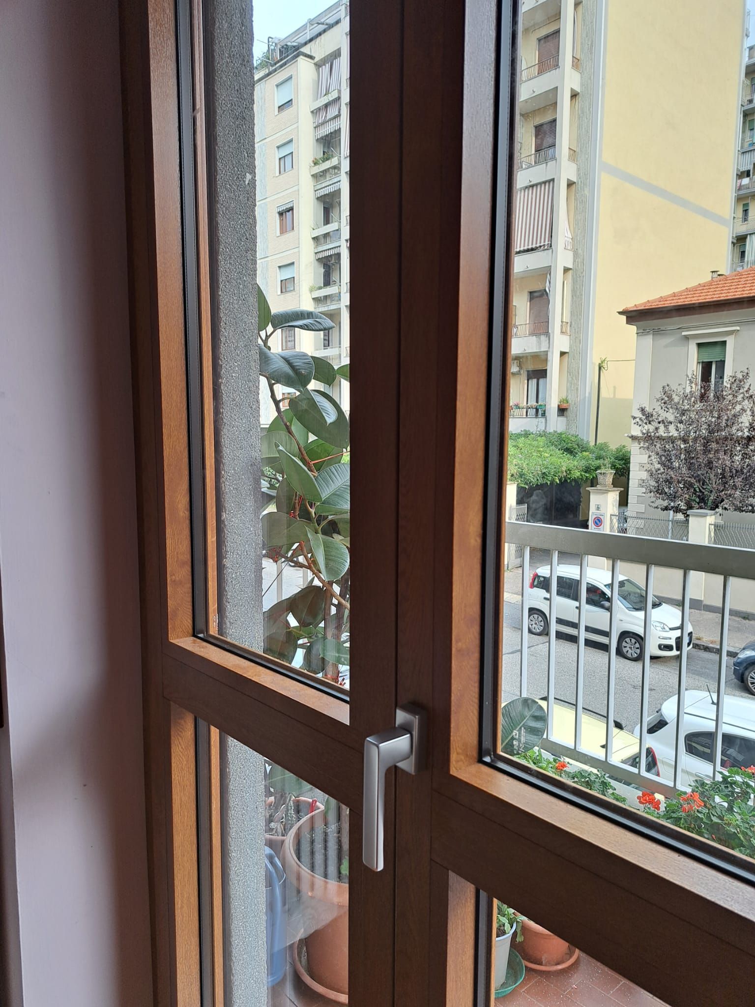Finestra con cornice in legno che si affaccia su una strada con automobili, balconi e condomini.