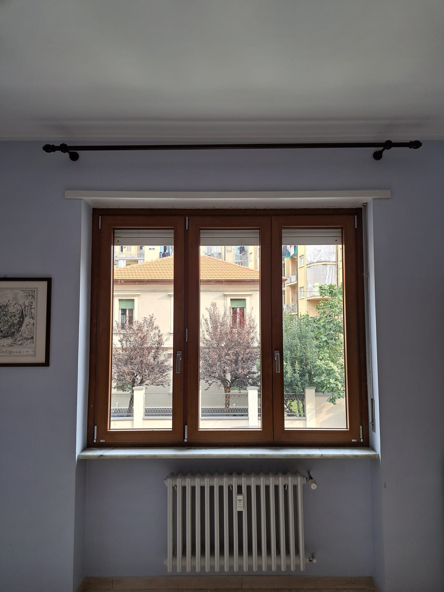 Una finestra con cornici marroni che si affaccia sull'esterno. Sotto c'è un termosifone.