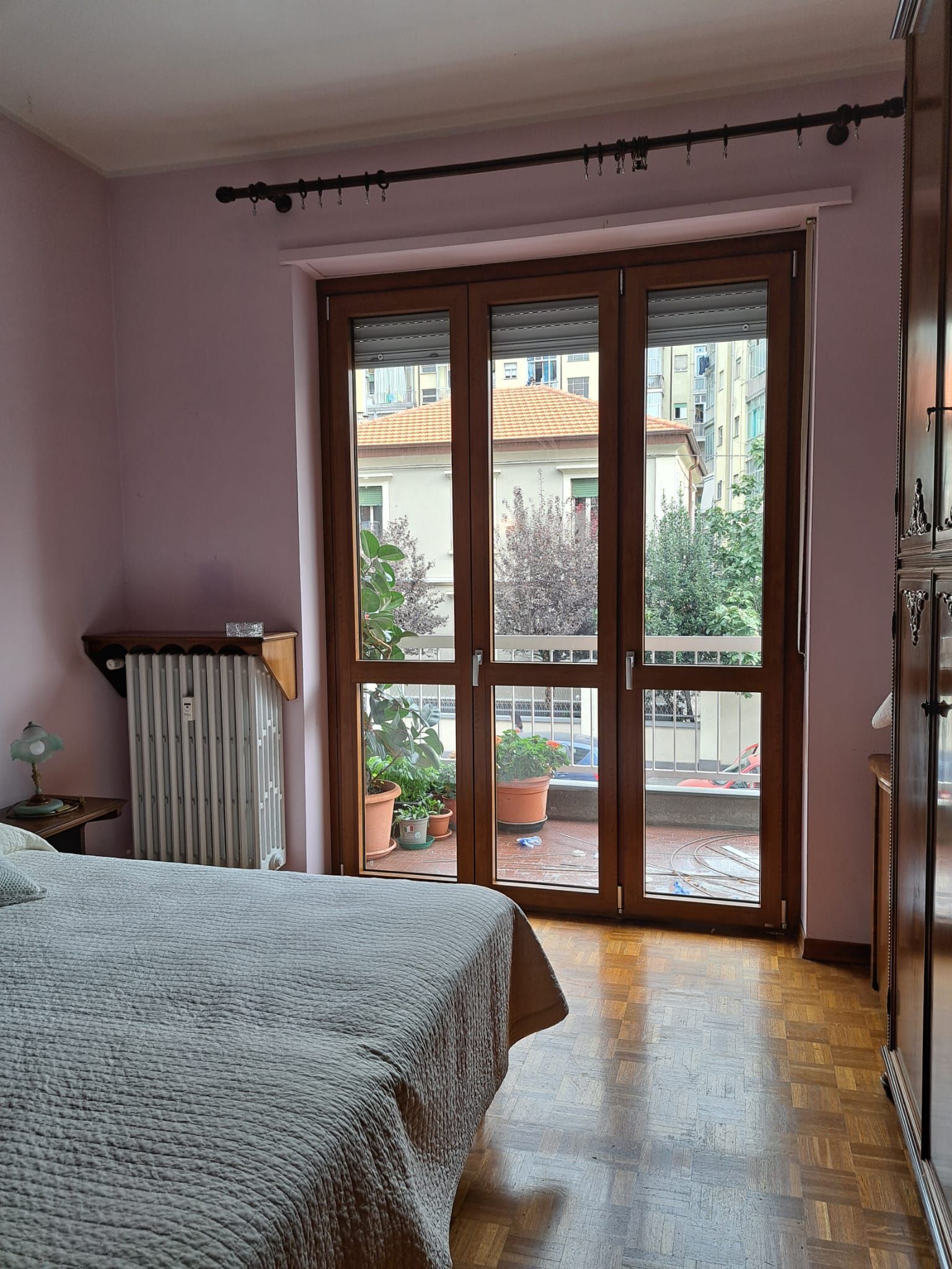 Camera da letto con porte in legno che danno su un piccolo balcone, pareti rosa, letto con copriletto bianco, pavimento in legno.
